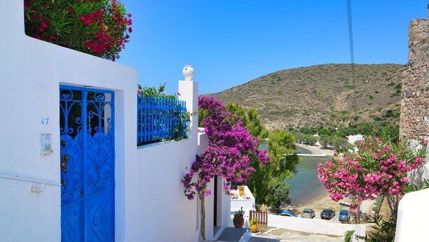 Un edificio blanco con puerta azul, buganvillas rosadas y vista a una colina.