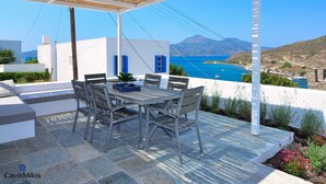 Un patio con mesa y sillas, con vistas a la costa y una montaña en la lejanía.