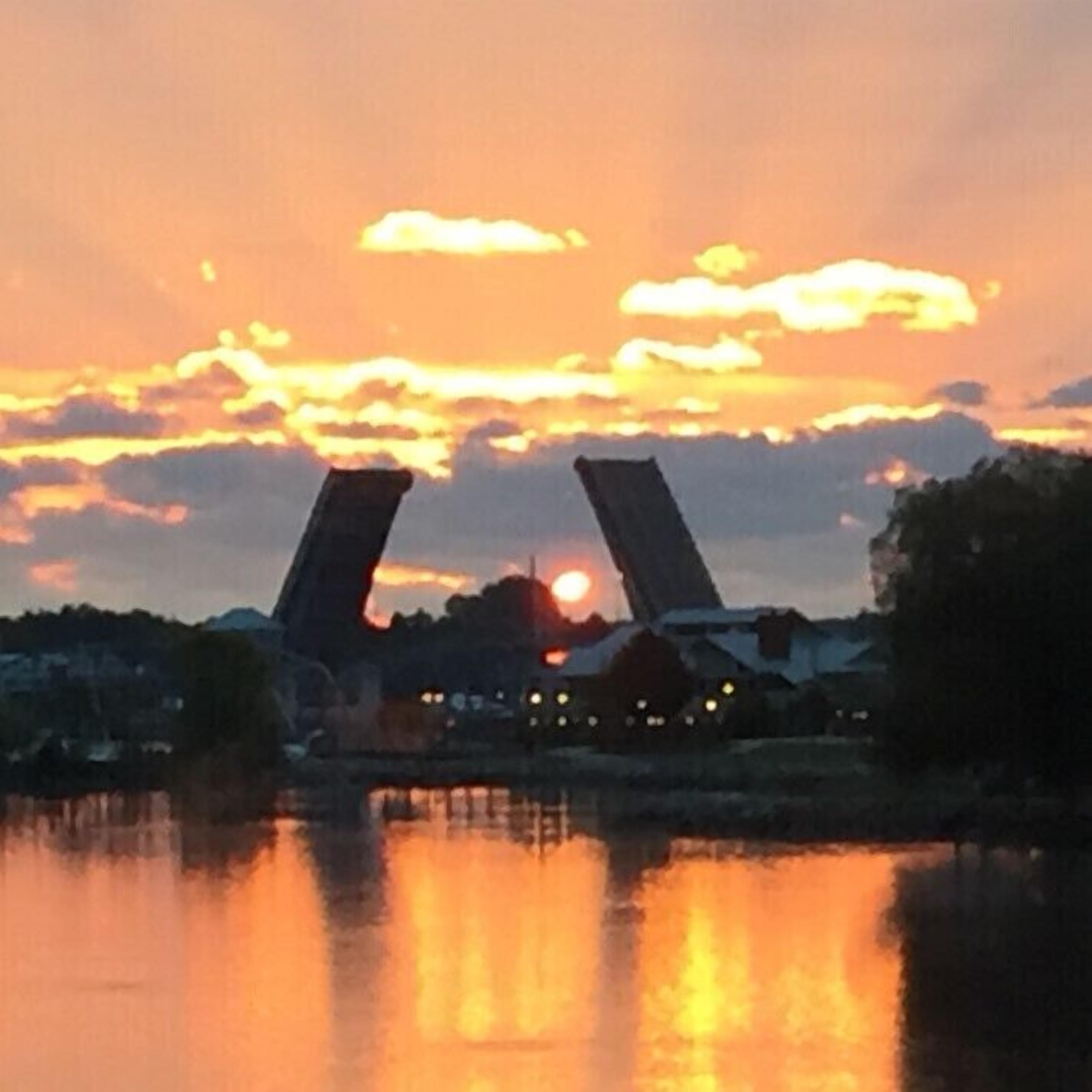 A sunset over a body of water with two large structures silhouetted against the sky.