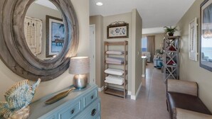 Un couloir avec un grand miroir, une commode bleue, une étagère avec des serviettes et une chaise.