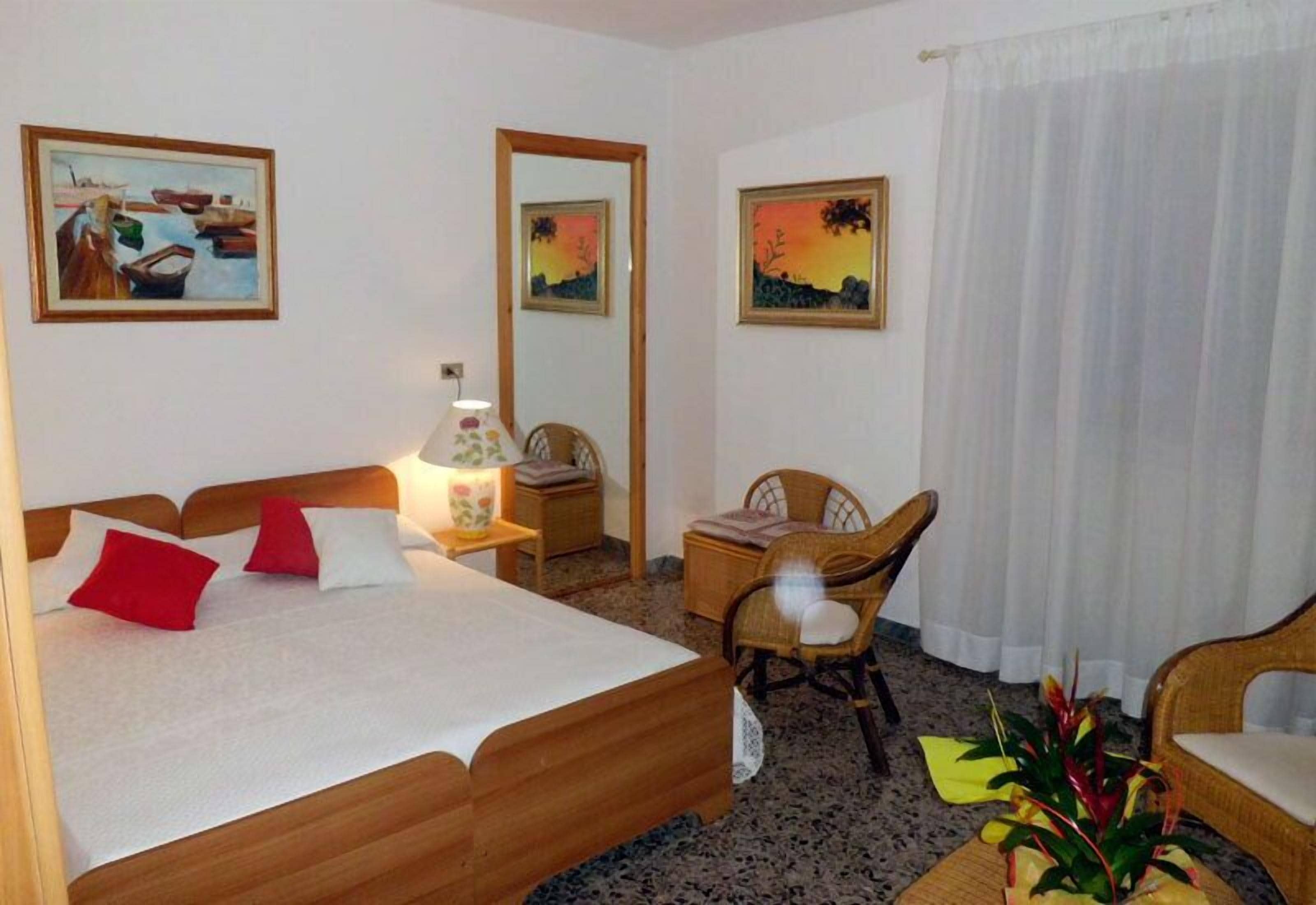 Ein Hotelzimmer mit einem Bett, einem Schreibtisch, zwei Stühlen, einem Spiegel und zwei Bildern an der Wand.