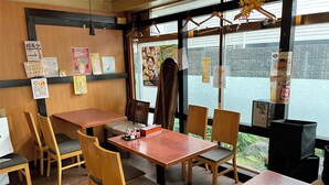 Interno di un ristorante con tavoli e sedie in legno, vista dalla finestra e diversi manifesti alle pareti.