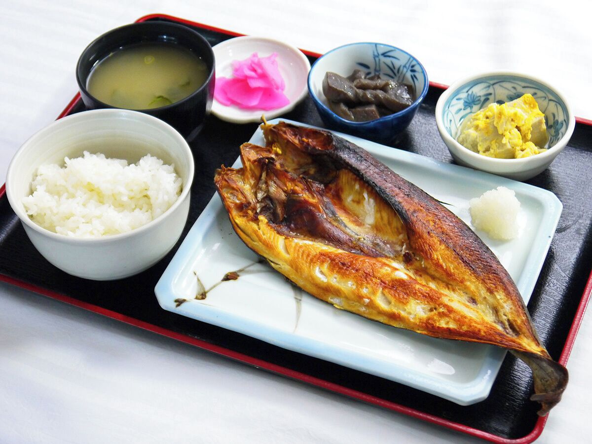 A tray with a whole grilled fish, white rice, and several small bowls containing different sauces and condiments.