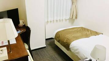 Quarto de hotel com cama, escrivaninha com luminária, cadeira, janela com cortinas e uma pequena mesa com uma xícara.