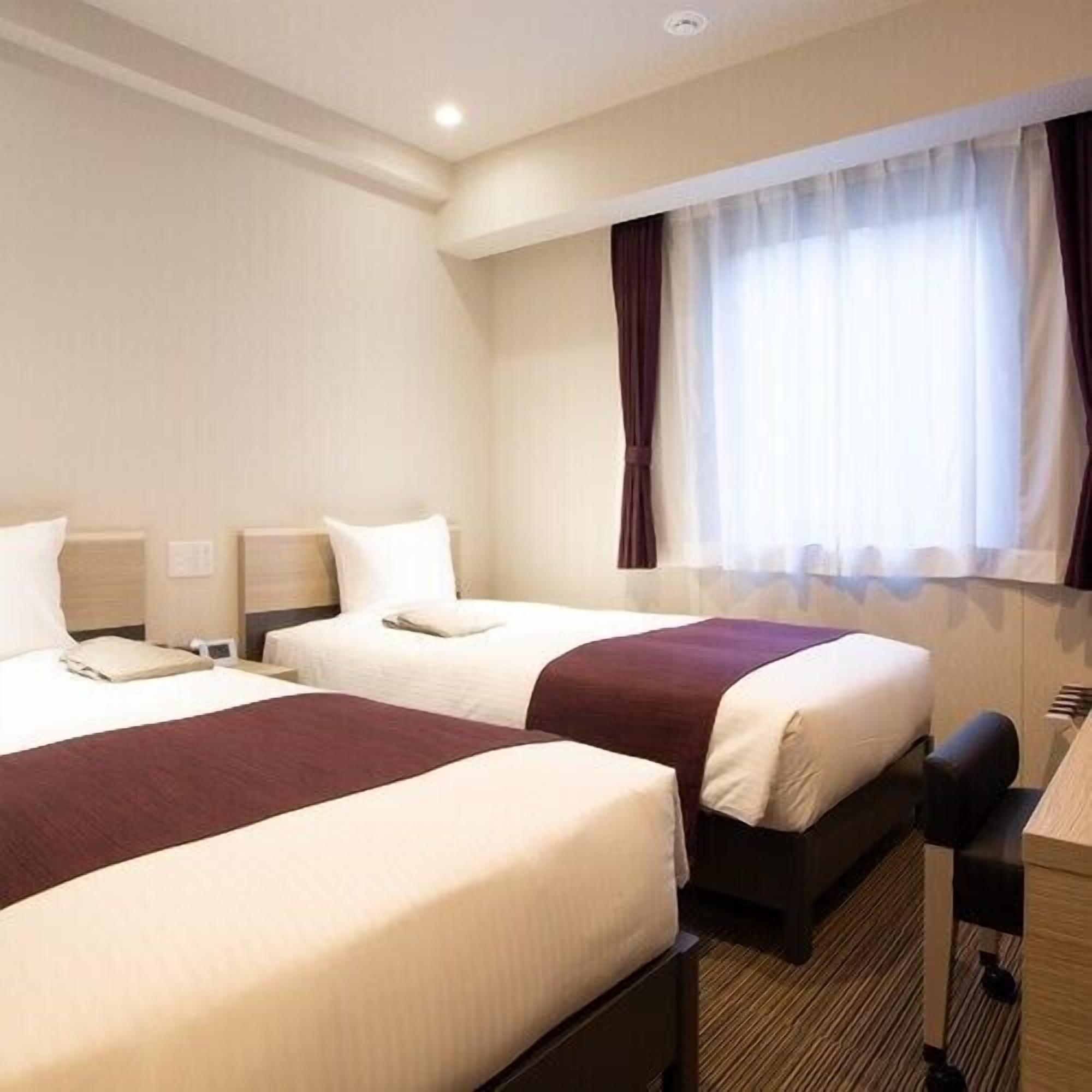 A hotel room with two beds, a desk, and a window with curtains.