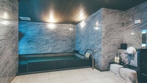 A modern bathroom with a marble wall, a glass-enclosed shower, and a sink area with toiletries. - Kuretake Inn Osaka Midosuji Honmachi (Osaka)