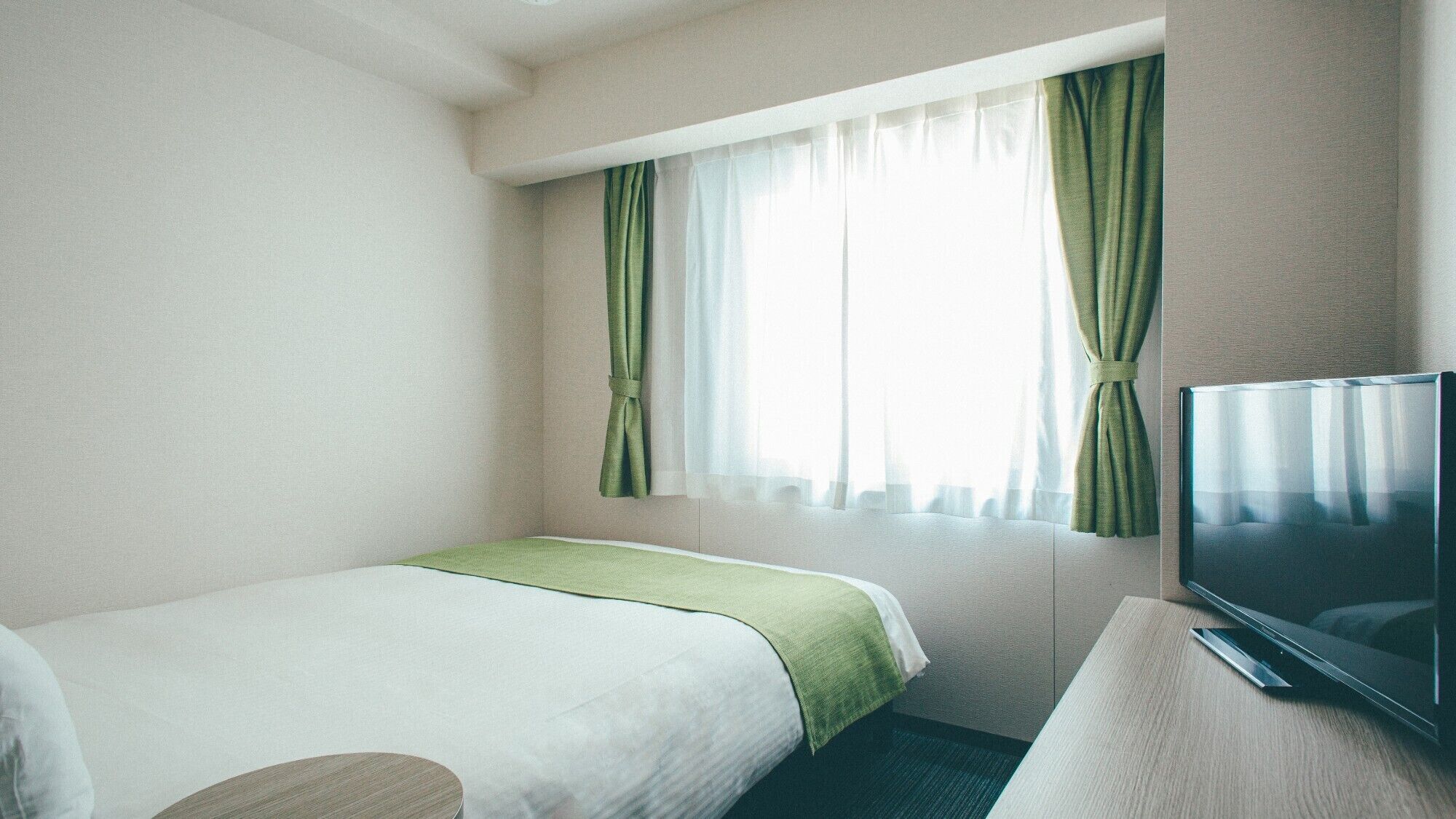 Ein Hotelzimmer mit zwei Betten, einem Fernseher und einem Fenster mit Vorhängen.