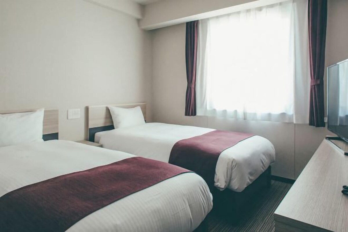Une chambre d’hôtel avec deux lits, un bureau et une télévision.