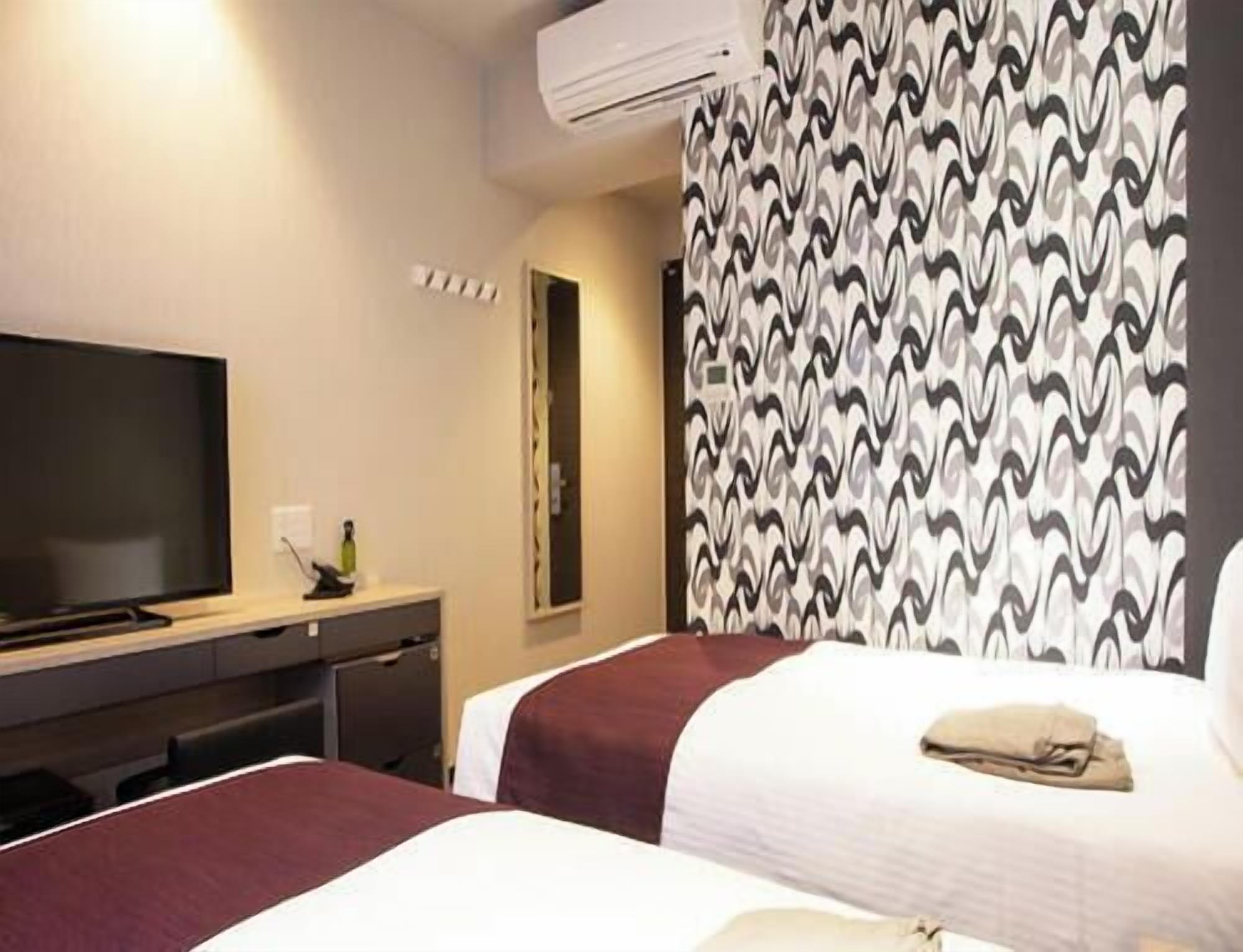 A hotel room with a bed, a desk with a television, and a patterned curtain.