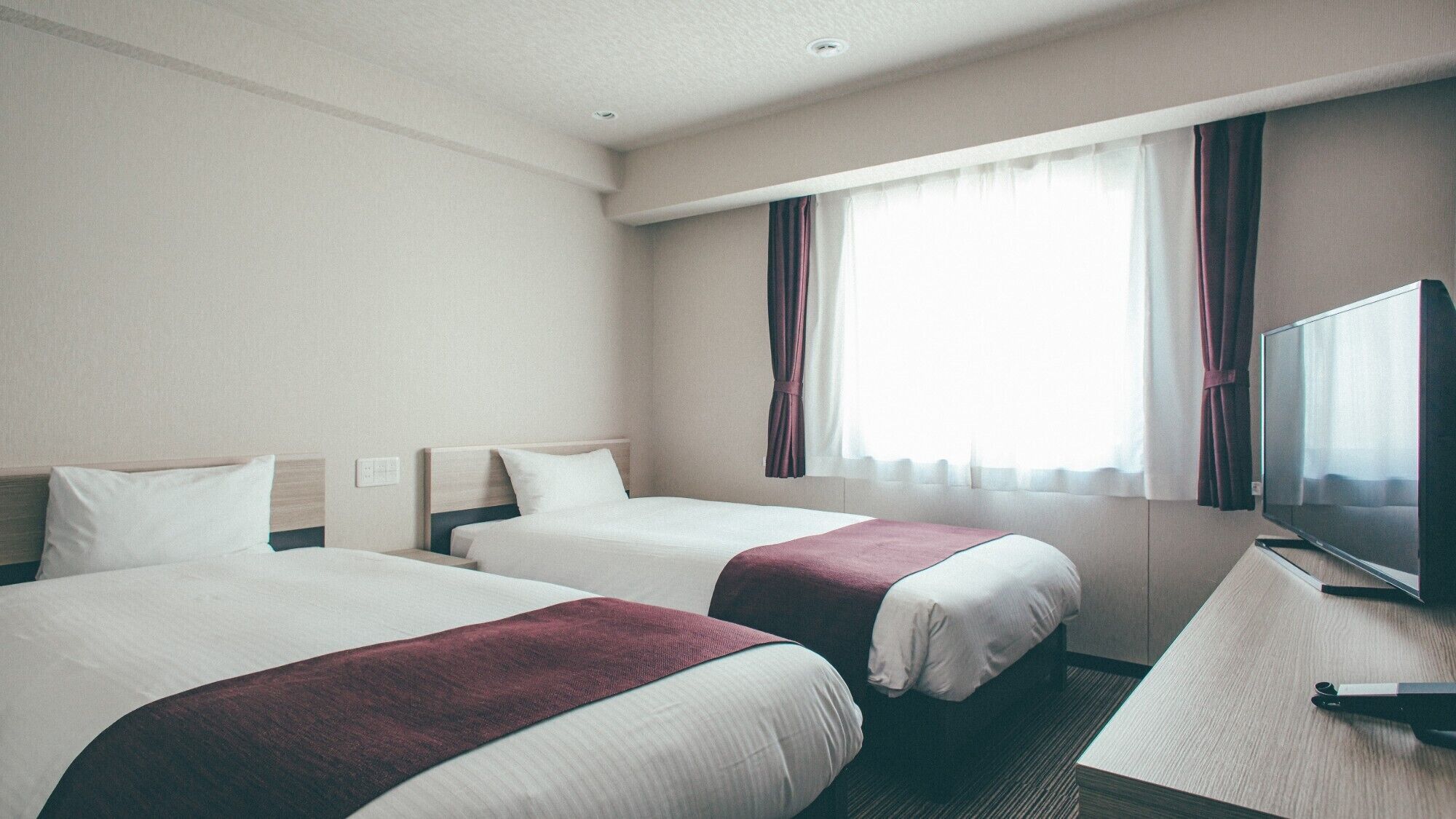 Ein Hotelzimmer mit zwei Betten, einem Fernseher und einem Fenster mit Vorhängen.