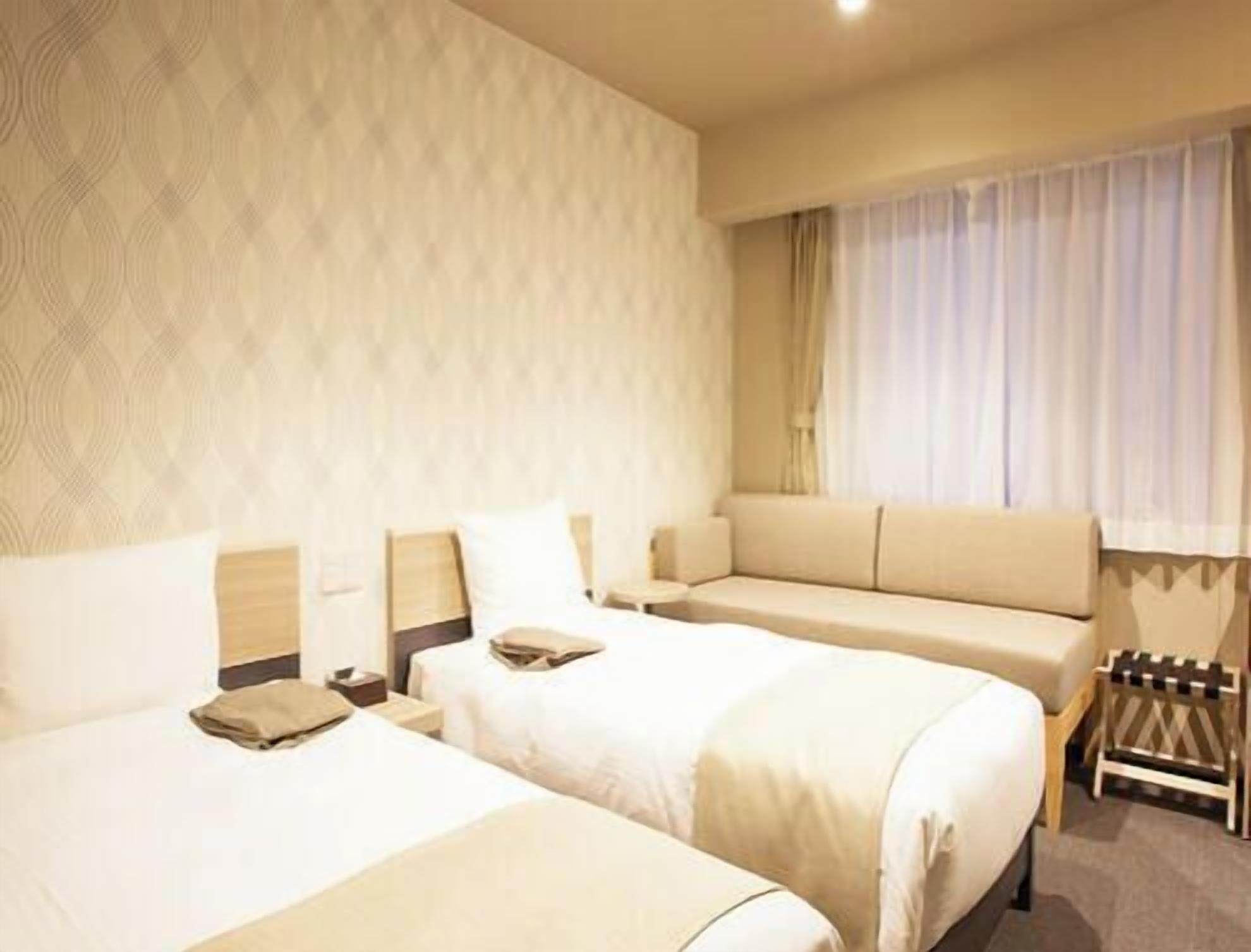 A hotel room with two beds, a sofa, a small table, and a window with curtains.