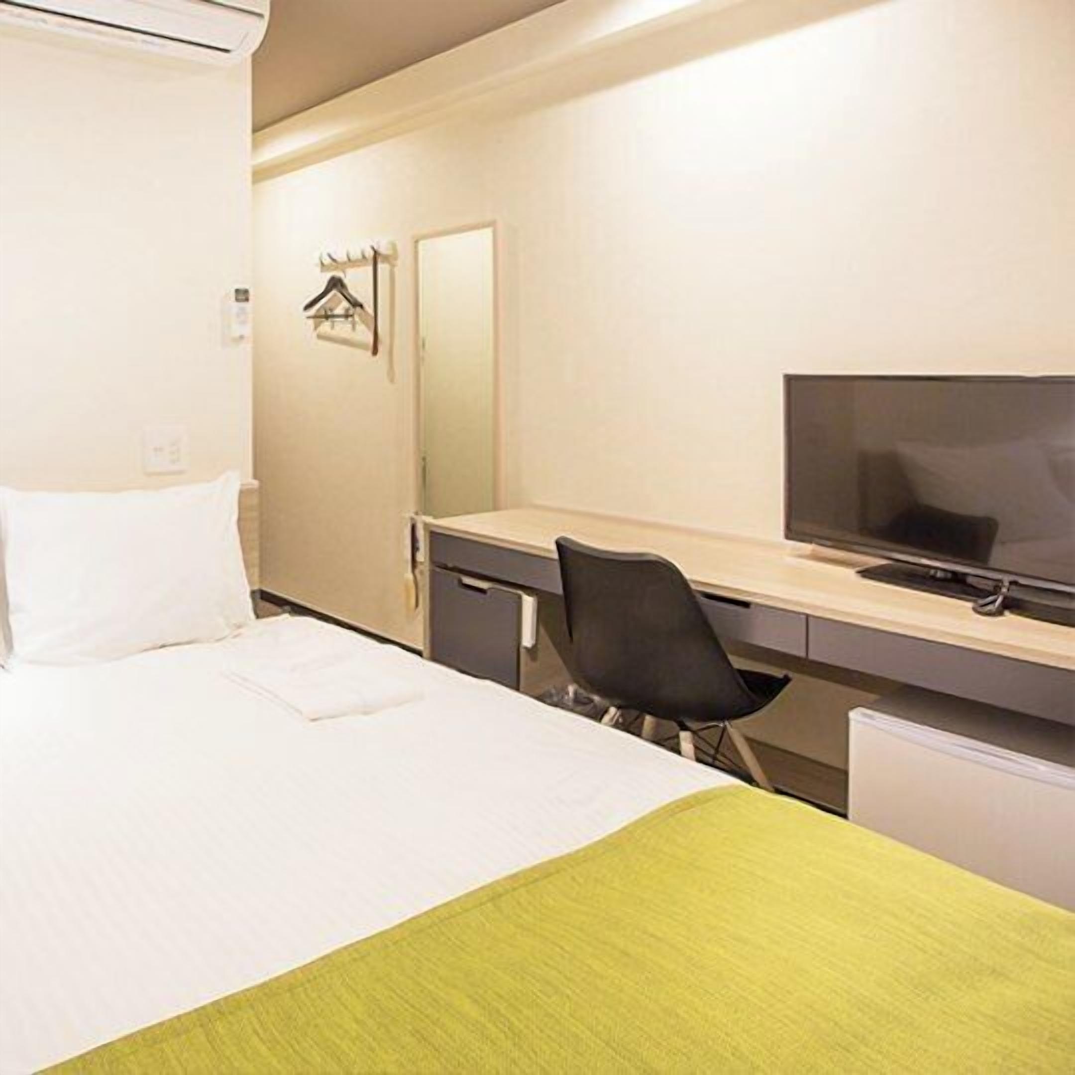 Ein Hotelzimmer mit Bett, Schreibtisch, Stuhl, Fernseher und Spiegel.
