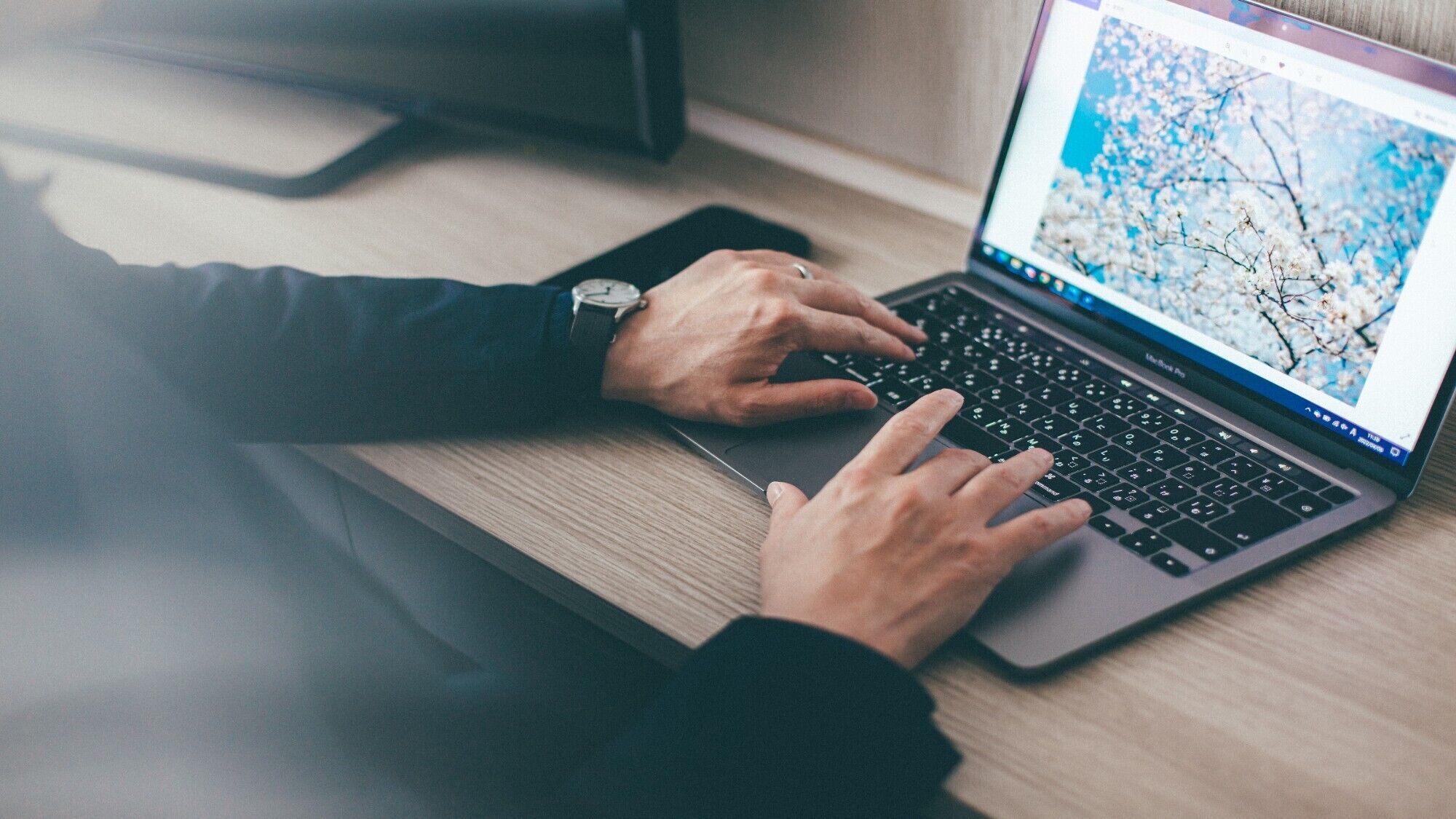 A person using a laptop on a wooden desk.