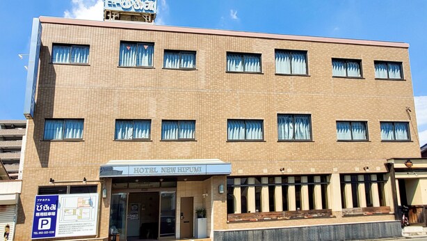 Un hotel de varios pisos con fachada de azulejos, una señalización sobre la entrada y un letrero de estacionamiento visible.