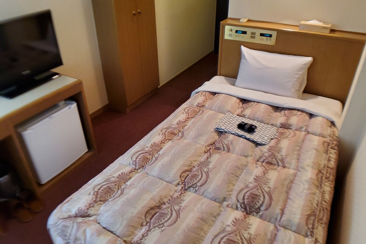 Une chambre d’hôtel équipée d’un lit, d’une télévision, d’un petit réfrigérateur et d’une armoire en bois.