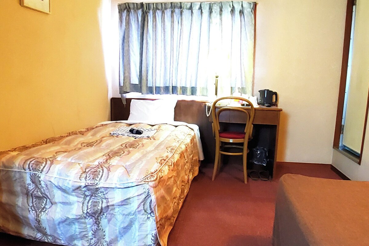 A hotel room with a bed, a desk, a chair, and a window with curtains.