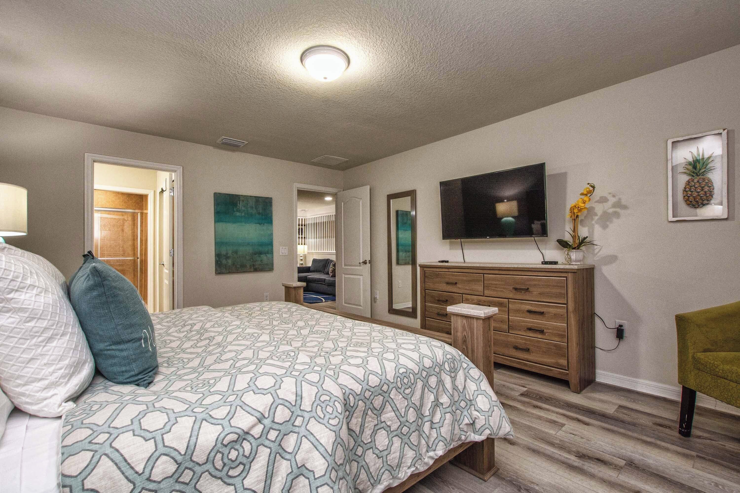 A bedroom with a bed, a dresser, a television, and artwork on the walls.
