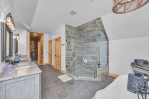 A modern bathroom with a glass-enclosed shower, a large bathtub, and a vanity with a marble countertop.
