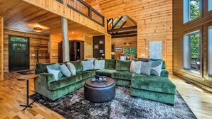 A spacious living area with a large green sectional sofa, a round ottoman, and a wooden floor.
