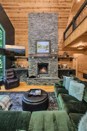 A cozy living room with a stone fireplace, leather seating, and a view of the outdoors.