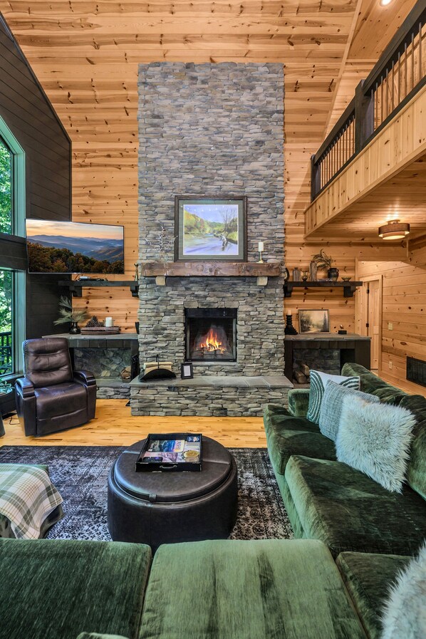 A cozy living room with a stone fireplace, leather seating, and a view of the outdoors.