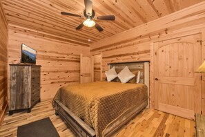 A wooden room with a bed, a ceiling fan, a dresser, and a door.