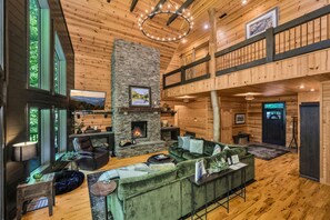 A spacious living area with a stone fireplace, a green sofa, and a television mounted on the wall.