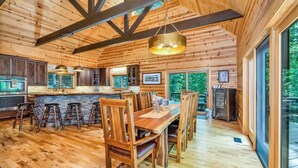 A spacious wooden interior with a large dining table, bar stools, and a kitchen area.