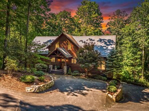 A log cabin with a metal roof, surrounded by dense forest.