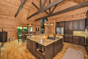 A spacious kitchen with a large island, wooden cabinetry, and a stone countertop. - 5 Acres to Roam | Stocked Game Room + Wet Bar  | Our Place to Paws (Lansing)