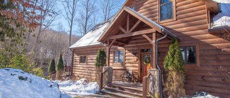 A log cabin with a porch, steps, and a stone wall.