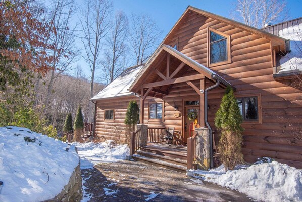 A log cabin with a porch, steps, and a stone wall.