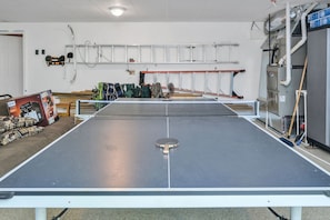 A ping pong table in a room with a ladder, chairs, and a table tennis paddle. - 5 Acres to Roam | Stocked Game Room + Wet Bar  | Our Place to Paws (Lansing)