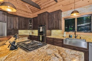 Una cocina con armarios de madera oscura, encimera de granito, electrodomésticos de acero inoxidable y una ventana con persianas.