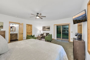 A bedroom with a large bed, a ceiling fan, a television, and a sliding glass door leading to a balcony. - 5 Acres to Roam | Stocked Game Room + Wet Bar  | Our Place to Paws (Lansing)