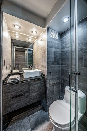 Une salle de bain moderne avec une douche à parois de verre, un lavabo blanc et des murs recouverts de carreaux foncés.