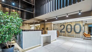 Een moderne receptiebalie met een receptie, een groot getal '200' op de muur, een kamerplant en een zithoek met banken.