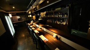 Un bar con una barra larga, suelo de madera y estantes llenos de botellas.