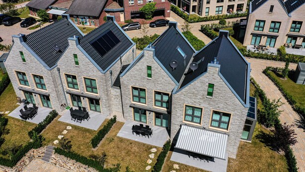 Een modern woongebouw met een gevel van natuursteen, meerdere ramen en een plat dak met zonnepanelen.