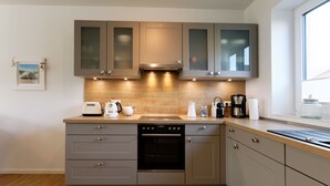 Een moderne keuken met grijze kastjes, een ingebouwde oven en een houten aanrecht.