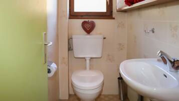 Une petite salle de bain avec des toilettes, un lavabo et une fenêtre située au-dessus des toilettes.