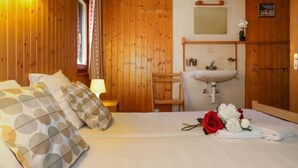 Ein Zimmer mit Holzboden, einem Bett, Kissen, einem Nachttisch, einer Lampe, einem Spiegel, einem Waschbecken und einem Blumenstrauß.