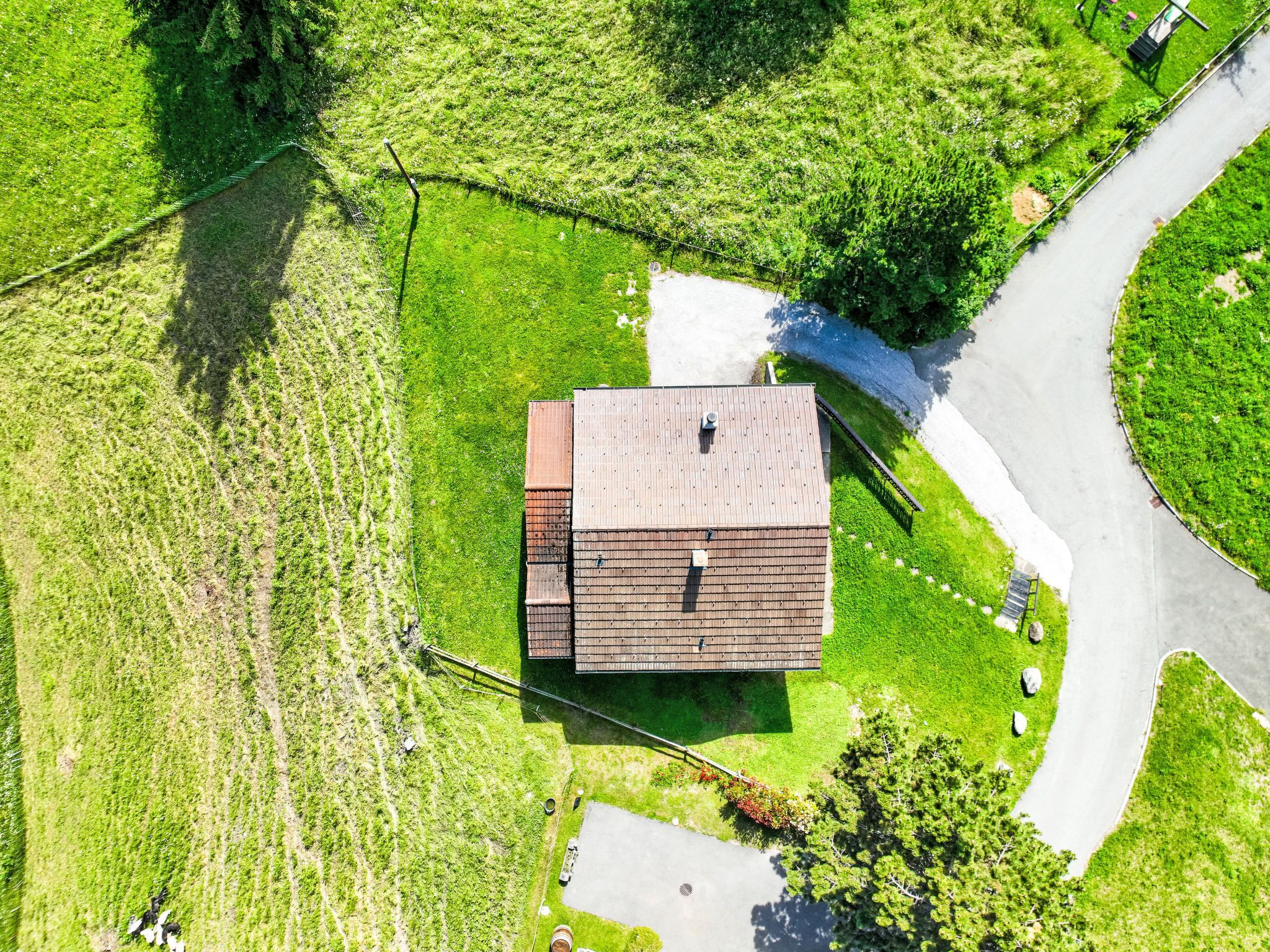An aerial view of a rural property with a single-story building, a paved driveway, and surrounding green fields.