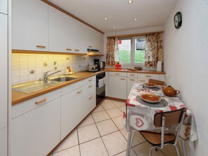 Cocina compacta con armarios blancos, encimera de madera, un lavamanos, estufa y una mesa de comedor para dos.
