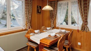 A wooden dining room with a table set for four, large windows with curtains, a radiator, and a hanging light fixture. - Strassscheuer by Interhome (Grindelwald)