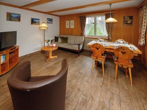 Un salon comprenant un canapé, une table à manger avec des chaises, un meuble pour la télévision et une lampe.