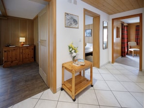 A hallway with a wooden cabinet, a small table with a vase of flowers, and a bed in the background.