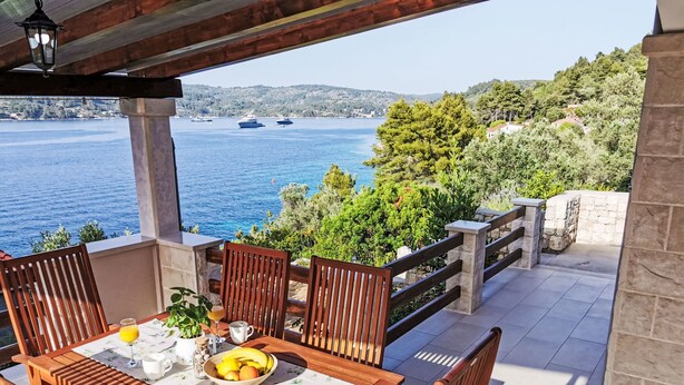 A wooden table with chairs and a bowl of fruit, overlooking a body of water with boats and greenery. - Vacation home Flora by Interhome (Korcula/Vela Luka)