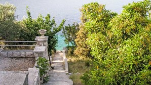A stone staircase leading down to a body of water, surrounded by lush greenery and a clear view of the lake. - Vacation home Flora by Interhome (Korcula/Vela Luka)