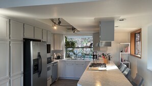 A modern kitchen with white cabinets, a stainless steel refrigerator, a built-in oven, a gas stove, and a large window providing natural light. - South Whidbey with water view, beach and hiking  (Clinton)